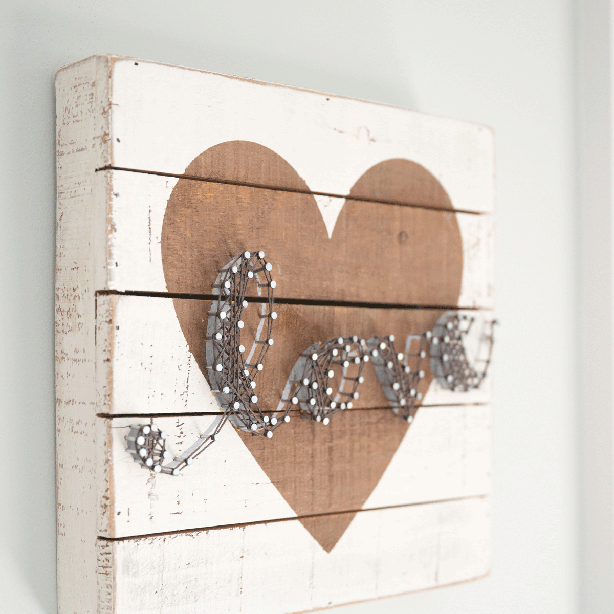 A rustic wood panel with 'love' spelled in wire on a whitewashed heart.